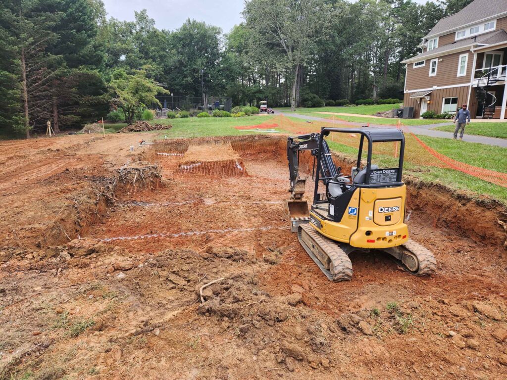 Excavator digging an inground swimming pool foundation during pool excavation and site preparation in Central Virginia.