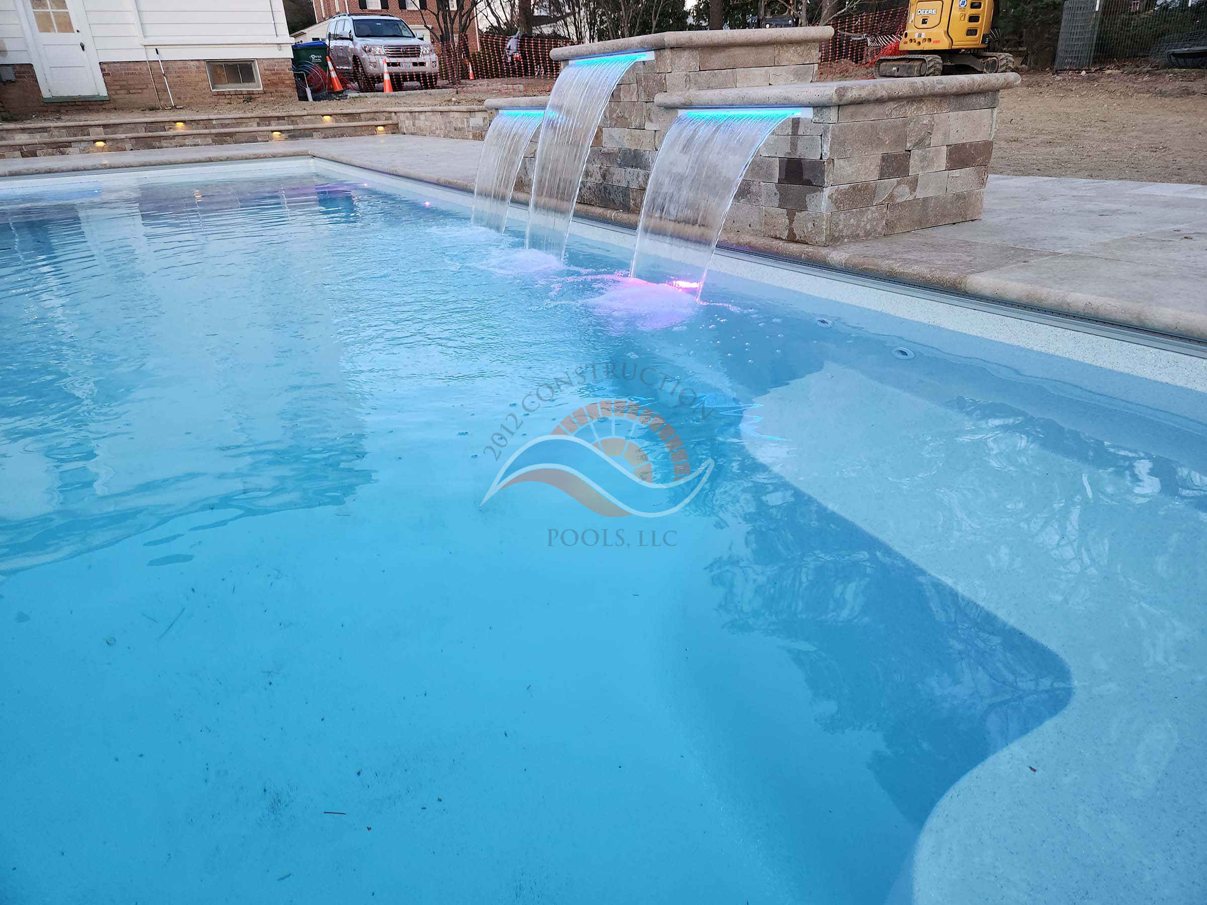 Fiberglass swimming pool with three sheer descent waterfalls and color LED lights flowing from a raised wall into the pool.