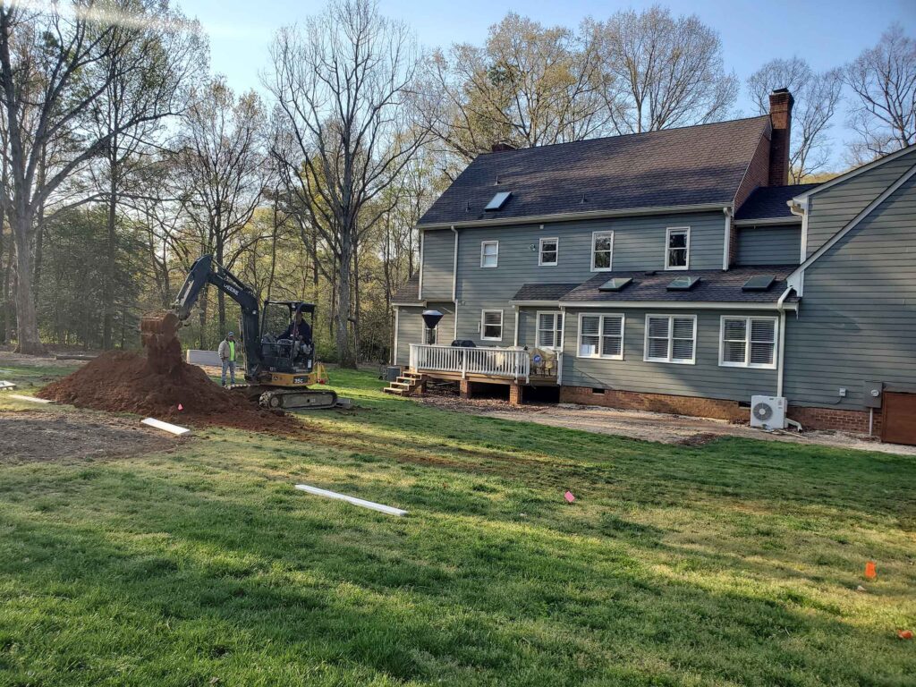 Excavator and crew preparing a backyard pool site during inground pool layout and site preparation in Central Virginia.