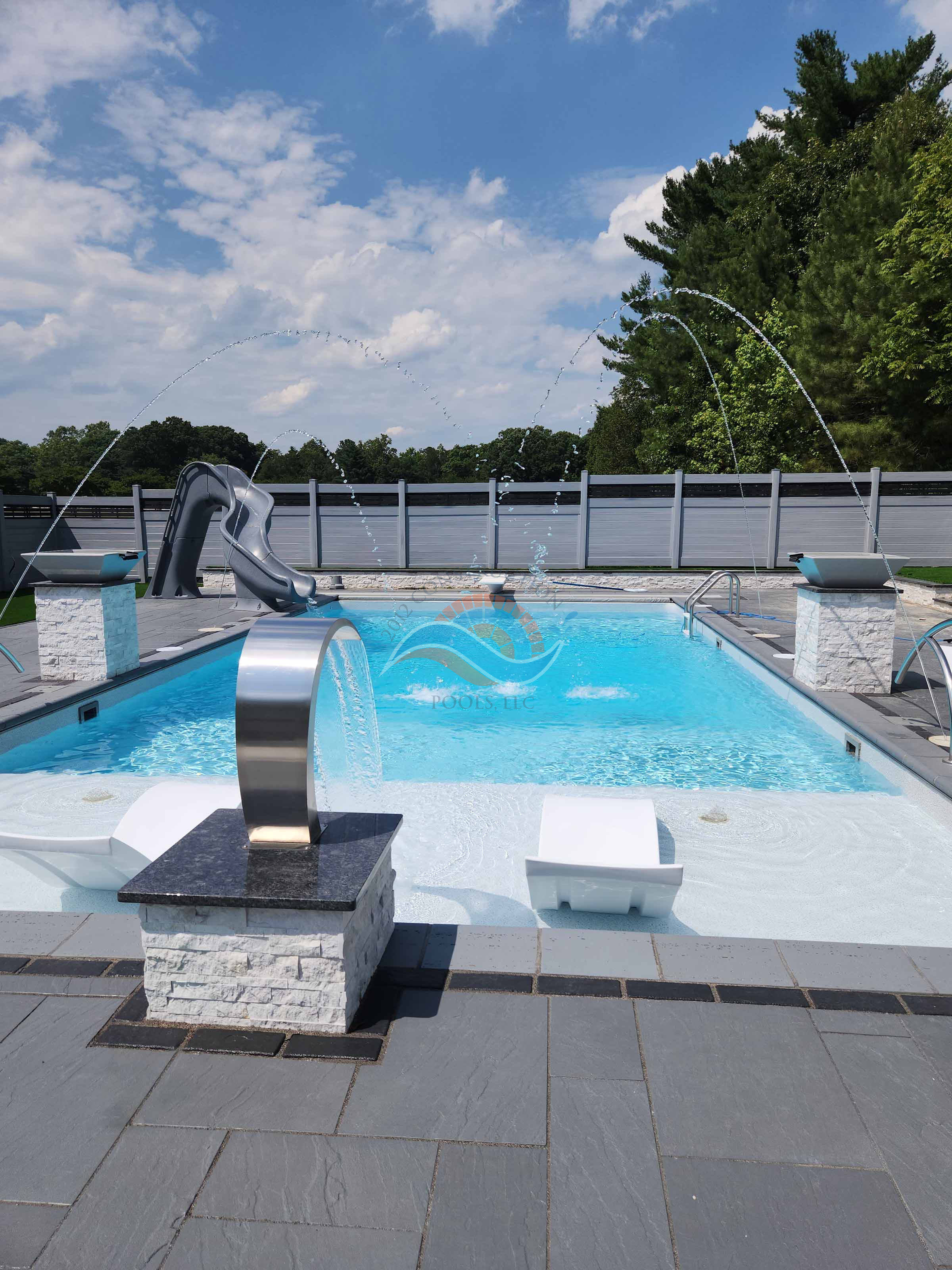 Vinyl liner inground pool with tanning ledge, deck jets, stainless waterfall spillway, and slide on a paver patio.