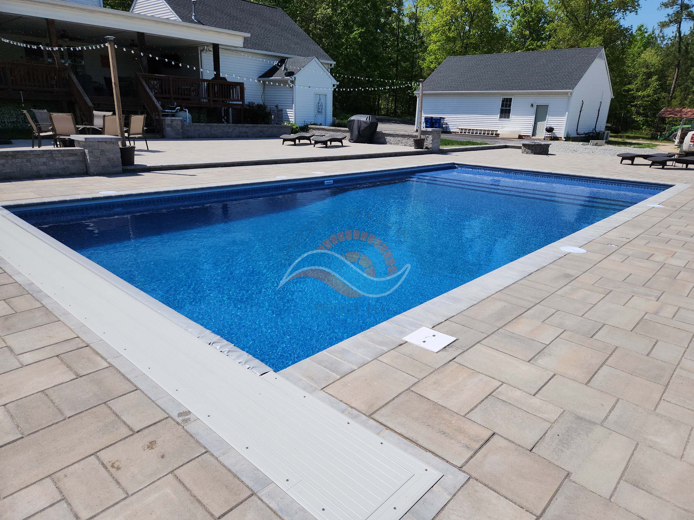 Vinyl liner inground swimming pool with automatic safety cover track and large paver pool deck at a residential backyard.